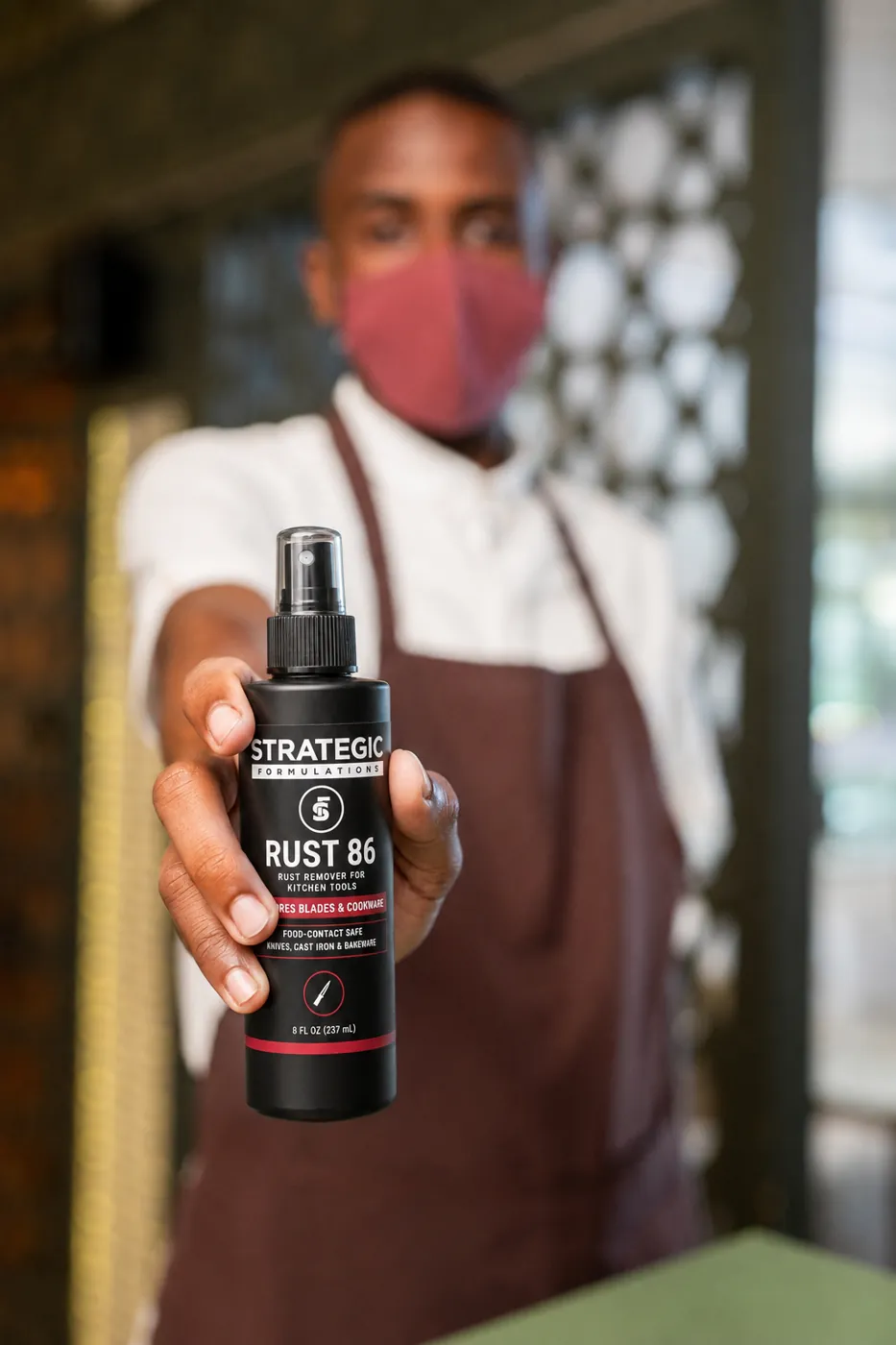 A chef holding up a bottle of RUST 86 in a restaurant kitchen